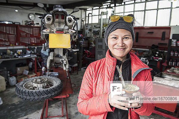 Porträt einer Frau  die in einer Motorradmechanikerwerkstatt Mate-Tee trinkt