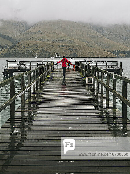 Frau in roter Jacke läuft fröhlich am Port Levy Jetty  NZ