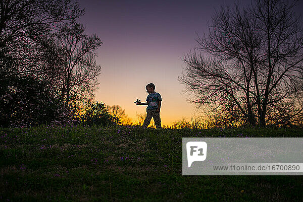 Kleiner Junge spielt Flugzeug Silohette Sommer Sonnenuntergang lila gelb