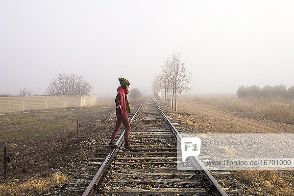 Side view of a girl balancing on train rail while walking