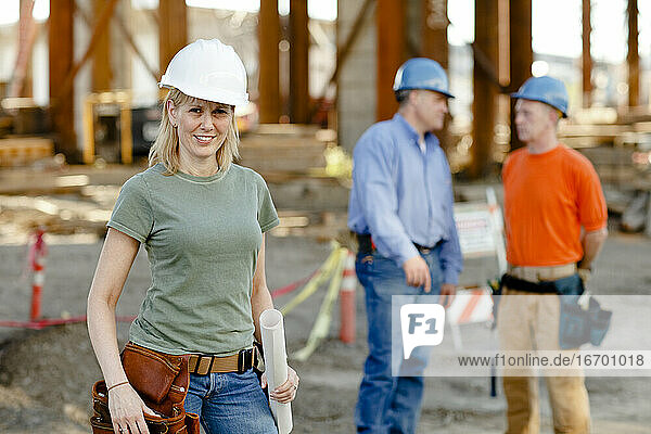 Porträt einer Bauarbeiterin mit zwei Arbeitern dahinter