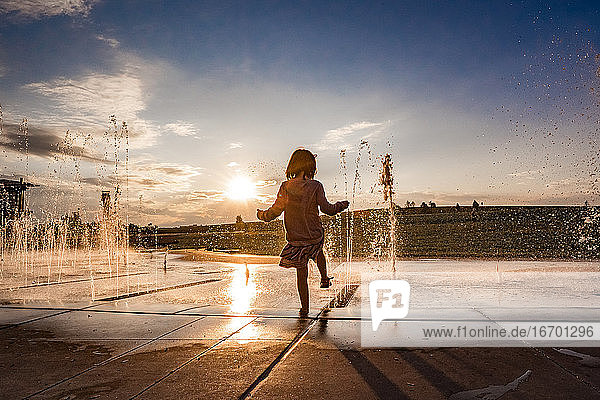 young girl hold her foot in the water at a splash pad at sunset