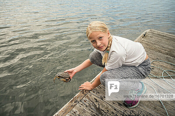 Blondes Mädchen mit Zopf hält eine Krabbe auf einem Holzsteg