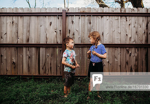 Zwei junge Kinder stehen draußen und unterhalten sich  bedeckt mit Schlamm