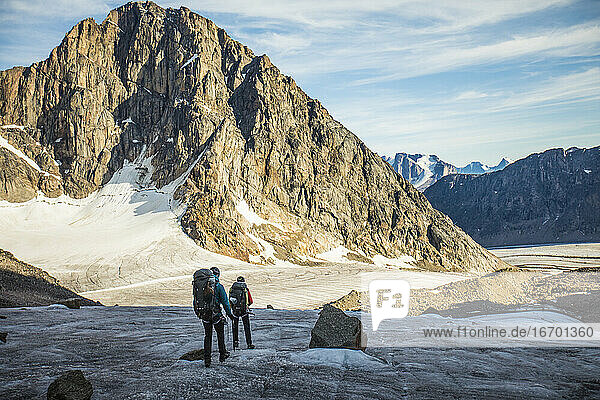 Zwei Rucksacktouristen überqueren einen Gletscher unterhalb einer Bergkette.
