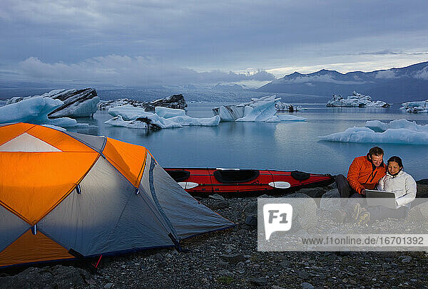 Pärchen schaut auf Laptop auf Campingplatz an Gletscherlagune in Island