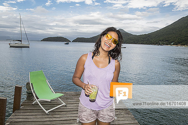 Frau mit Getränk in der Hand auf dem Pier der tropischen Insel Ilha Grande