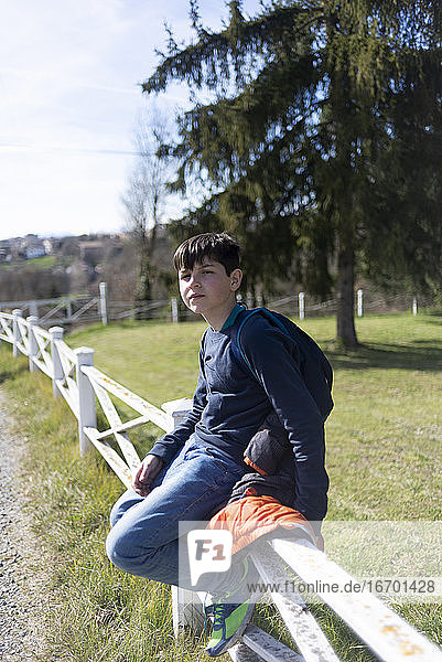 Junger Teenager  männlich  sitzt auf dem Lande am Zaun und schaut in die Kamera