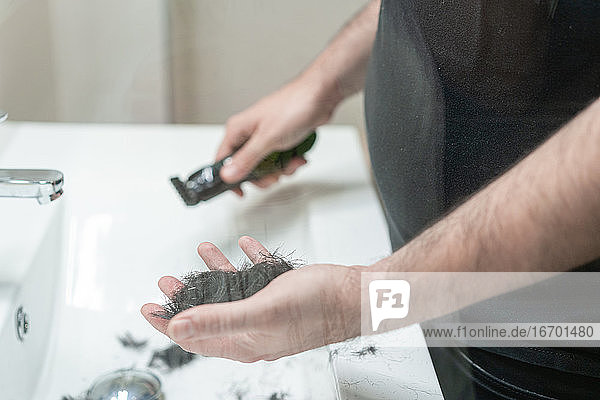 Selbsthaarschnitt. Ein anonymer Mann hält mit seiner Hand Haarsträhnen im Badezimmer
