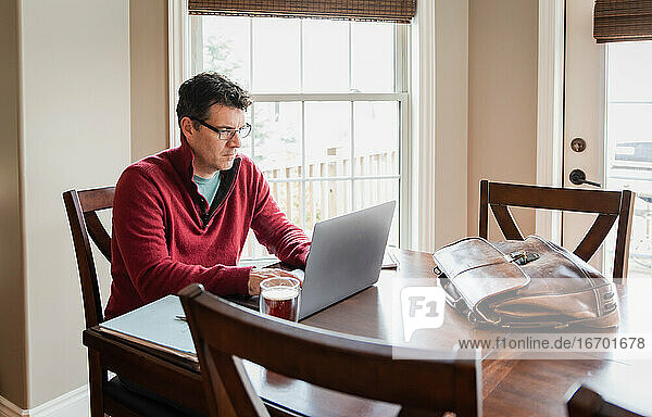 Mann mit Brille arbeitet von zu Hause aus an einem Computer am Esstisch.