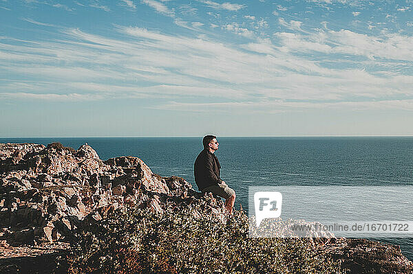 Young man looking at ocean from cliff in Portugal in summer