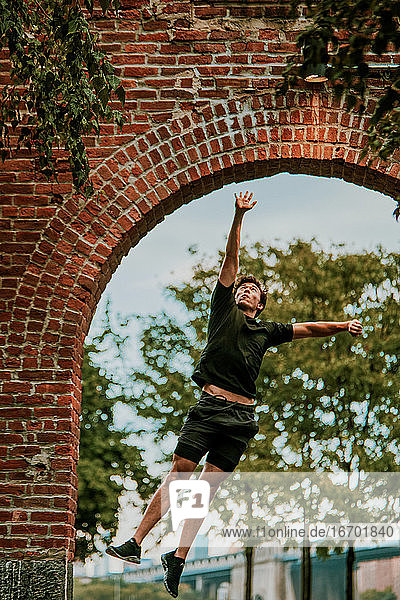 Junger Mann springt im Freien im Park hoch.