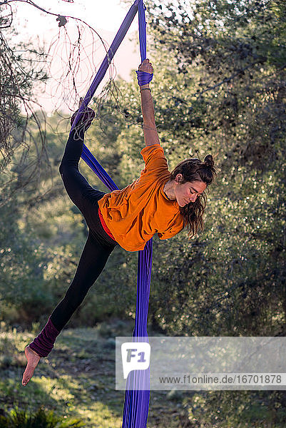 Junges Mädchen  Akrobatin. Übt Seiltanz in der Luft. Frau macht Zirkuskunststücke mit Kleidung im Wald. Figürliche Kopfhaltung.
