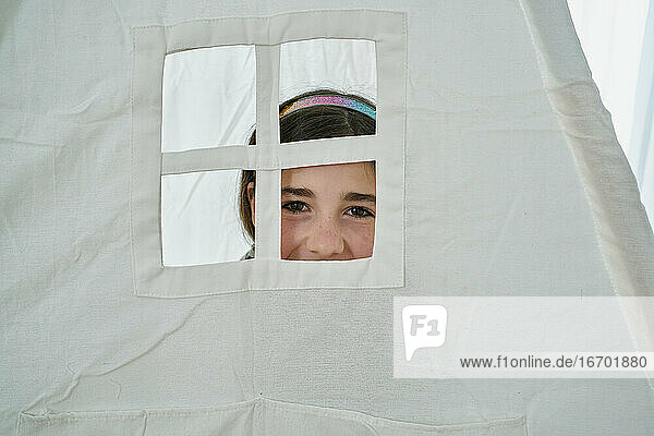 Junges Mädchen schaut durch ein Fenster auf ein weißes Tipi-Zelt. Kreatives Konzept
