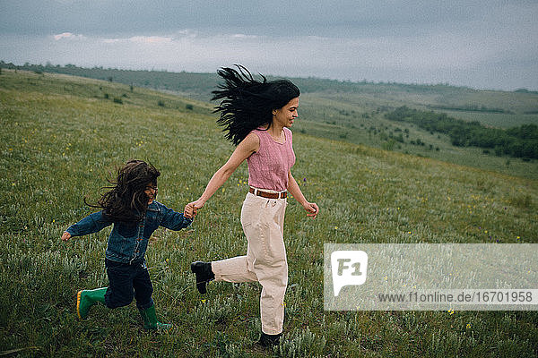 mom and daughter running down hill in countryside
