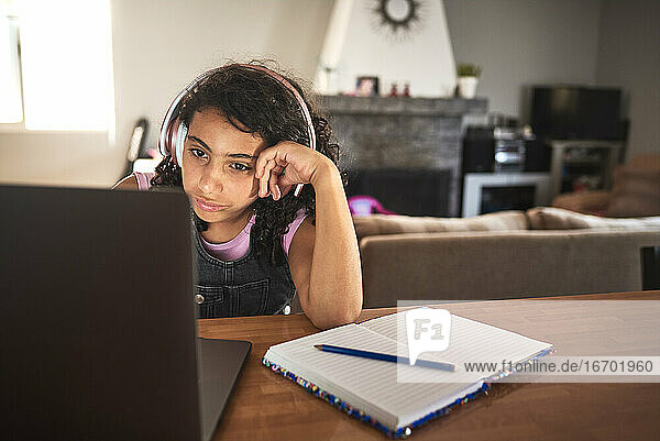Ein gelangweiltes Mädchen macht seine Hausaufgaben mit seinem Laptop
