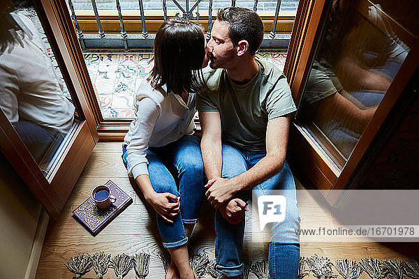 Draufsicht auf ein junges  intimes Paar  das sich zu Hause neben einem Fenster mit Balkon küsst.