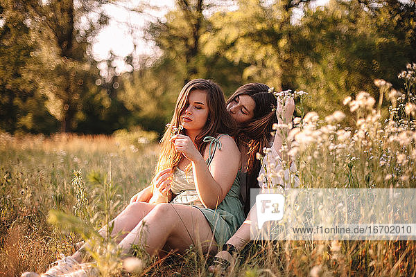 Lesbian couple sitting in field of flowers in forest during summer