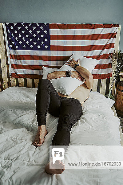 Ein junger Mann umarmt ein Kissen auf dem Bett mit der amerikanischen Flagge.