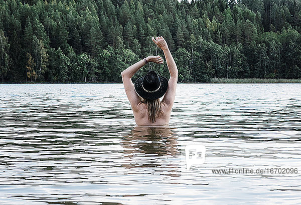 Eine Frau stand nackt im Wasser und tanzte mit einem Hut auf dem Kopf.