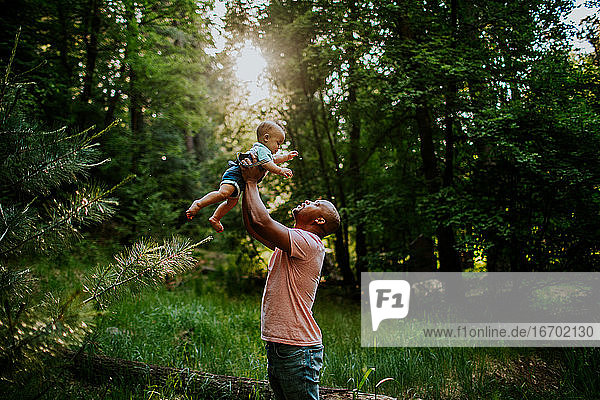 Dad holding infant son up in the air in the middle of forest