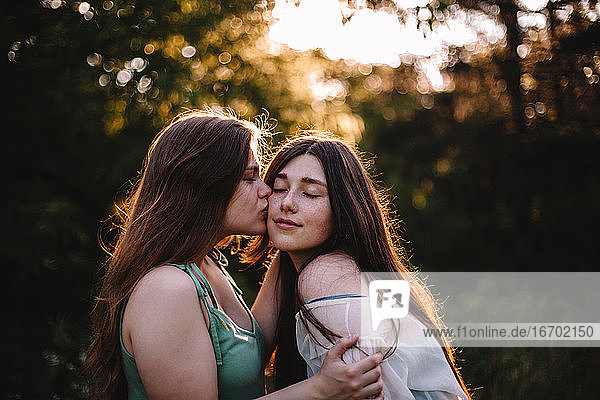 Young woman kissing her girlfriend on the cheek in forest in summer