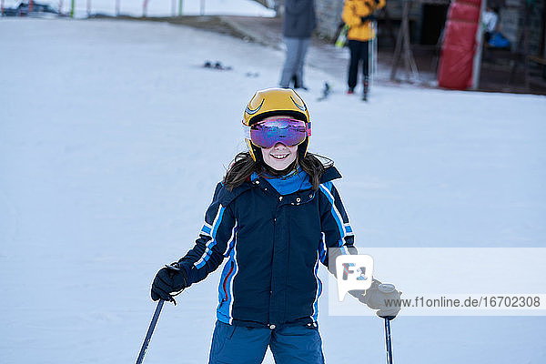 Mädchen mit Helm und Brille schaut lächelnd auf einer Skipiste