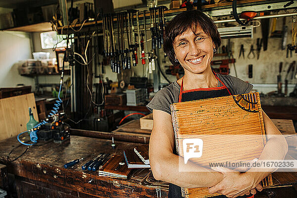 Künstlerin hält ihr Holzkunstwerk und lächelt in einer Werkstatt