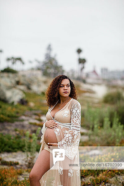Junge schwangere Frau posiert am Strand in transparentem Kleid