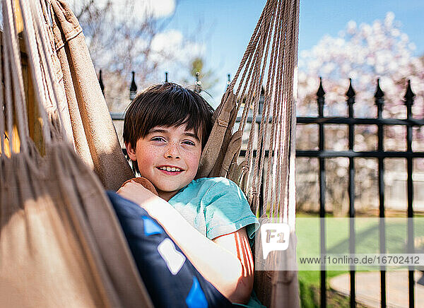 Happy boy relaxing in a hammock in a backyard on a summer day.