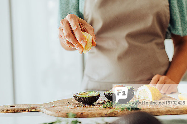 Weibliche Hände  die bei der Zubereitung einer gesunden Mahlzeit eine Zitrone auf einer Avocado auspressen