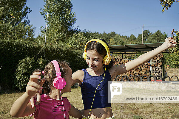 Little girls hugging and listening to music with yellow and pink headphones in the garden. Summer concept