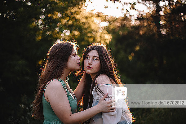 Young woman is about to kiss her girlfriend in forest during summer
