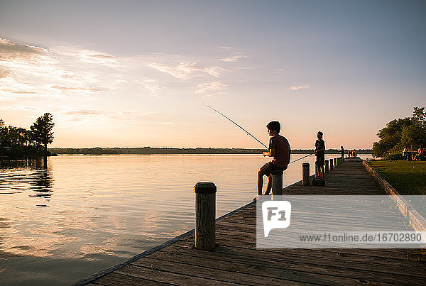 Jungen angeln am Steg eines Sees bei Sonnenuntergang in Ontario  Kanada.