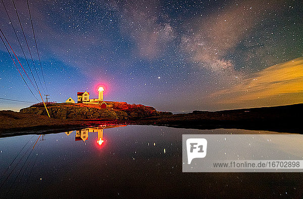 Lighthouse reflecting in water under the night sky milky way.