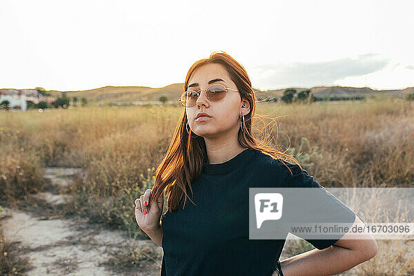 Teenager mit Sonnenbrille berührt Haar bei Sonnenuntergang in der Landschaft