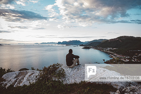 Wanderer sitzt auf einem Felsen und schaut auf Meer und Inseln