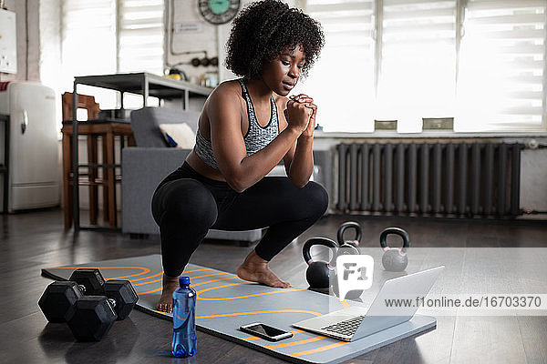 Afroamerikanische Sportlerin in der Hocke beim Online-Workout