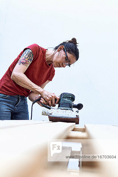 Junge Frau beim Polieren eines Holzbretts mit einer Schleifmaschine