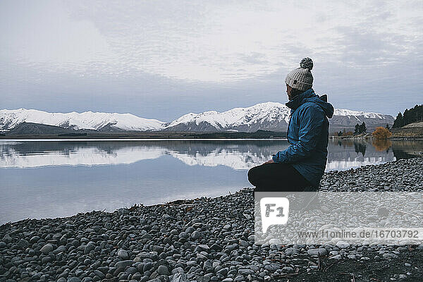 Junge Frau kniet am Lake Tekapo nieder und blickt auf die Südalpen