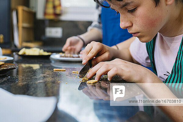 Junger Teenager schneidet Kekse mit einem Messer auf der Arbeitsplatte in der Küche aus