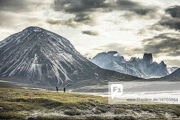 Silhouette von zwei Rucksacktouristen  die über einen dramatischen Bergpass wandern.