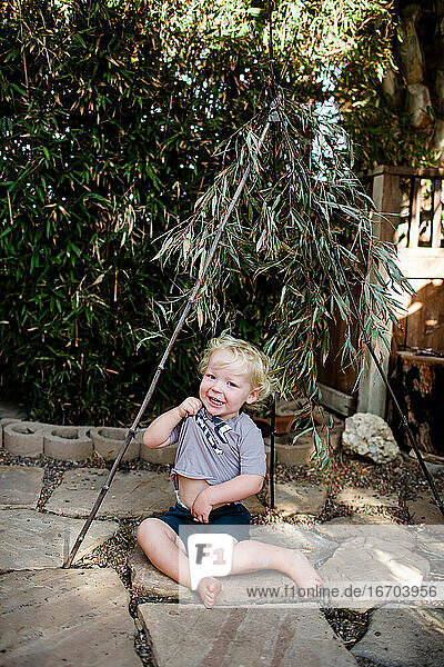Zwei Jahre alter Junge unter Bambus sitzend  lachend und spielend