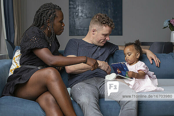 Multiracial family sitting with their daughter on a couch