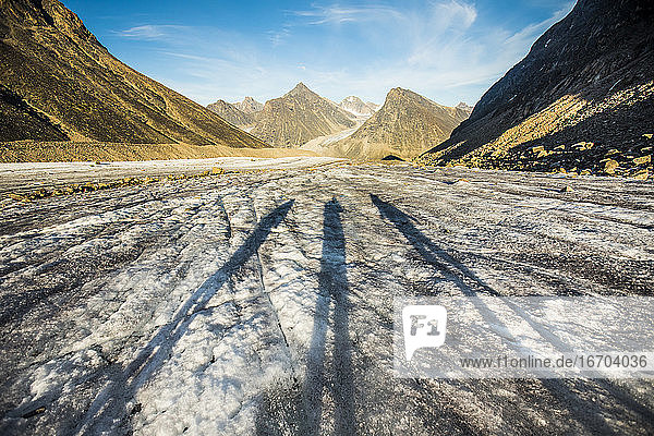 Schatten von drei Forschern auf einem Gletscher in den Bergen.