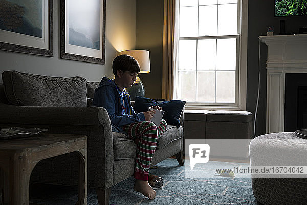 Seite Silhouette von Teenager Junge sitzt auf Couch Öffnen eines Briefes