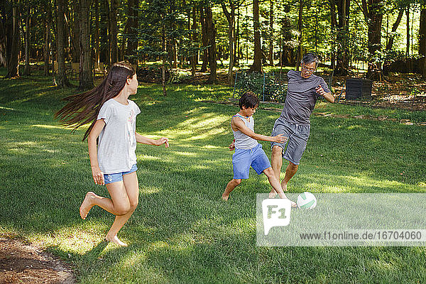 Ein Vater spielt mit seinen beiden Kindern barfuß im Garten Fußball