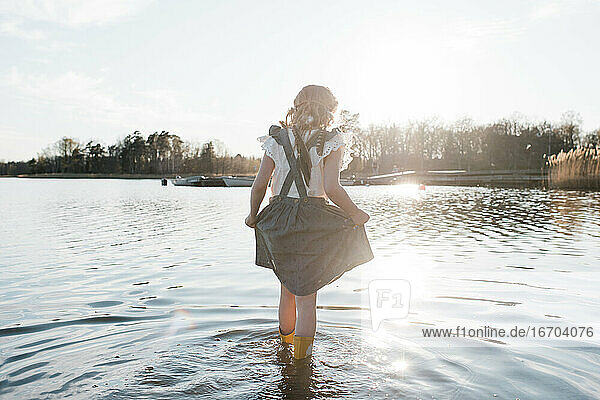 junges Mädchen  das in einem hübschen Kleid bei Sonnenuntergang durchs Wasser läuft
