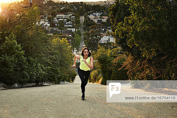 Full length of jogger running on road amidst trees during sunset
