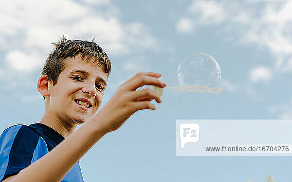 Junger weißer Junge zeigt eine Seifenblase im Freien mit Himmel im Hintergrund
